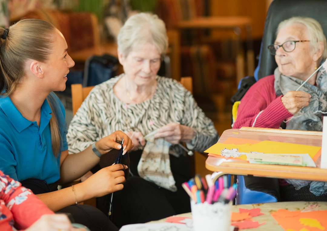 caregiver-assisting-elderly-women-with-knitting-activity-d394dkgojec